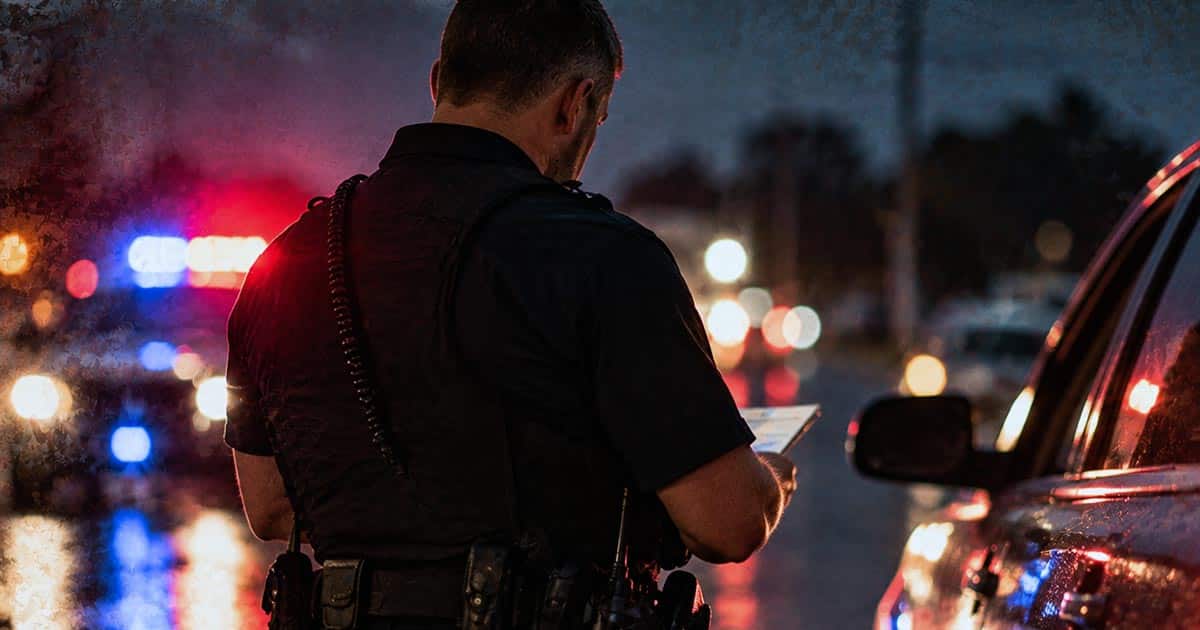 Police officer speaking with a driver during a nighttime traffic stop on a rural road
