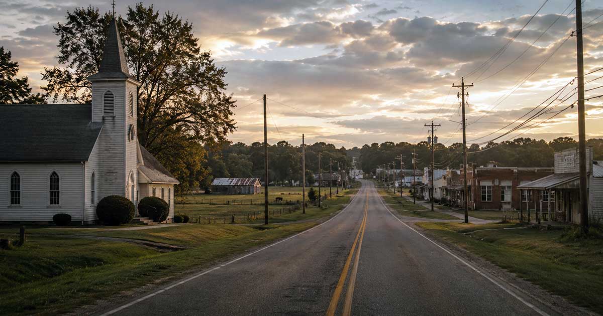 Two-lane road through a small Barbour County Alabama community with a church, fields, utility lines, and older buildings.